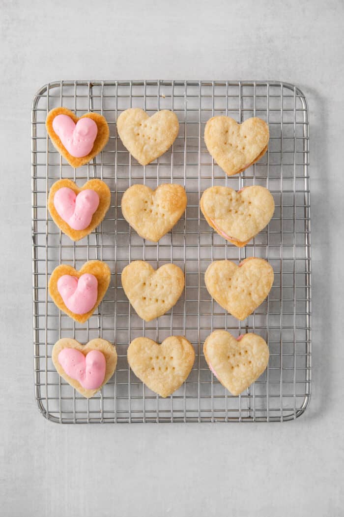 Cream wafter cookies, four topped with strawberry buttercream, on a wire rack.