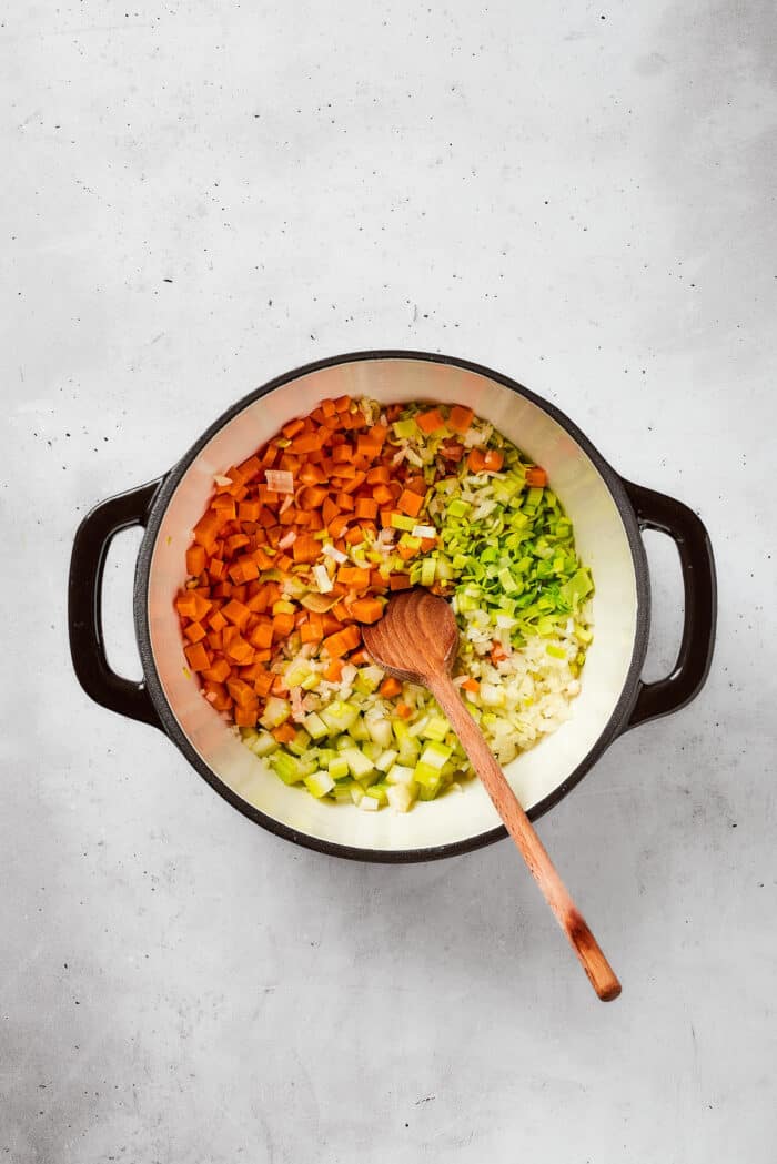 Vegetables including carrots and celery are added to a soup pot.