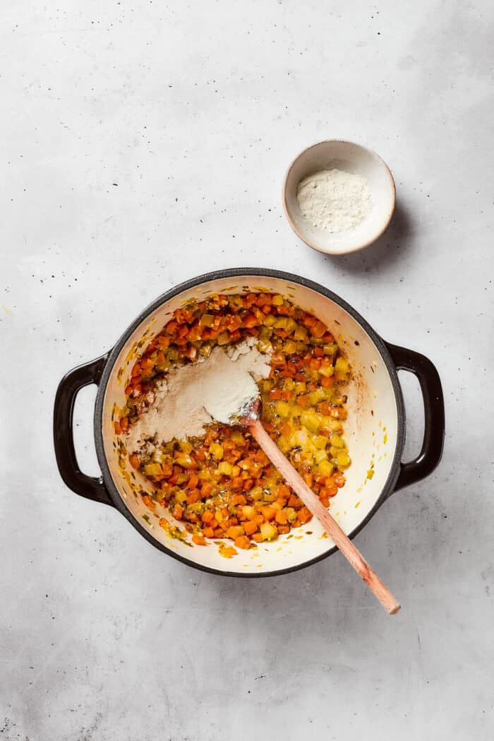 Flour is stirred into a pot of lemon chicken orzo soup.