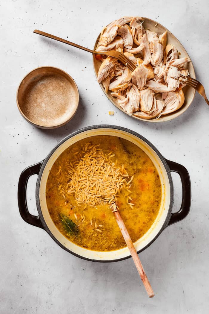 Dried orzo is added to a pot of lemon chicken orzo soup.