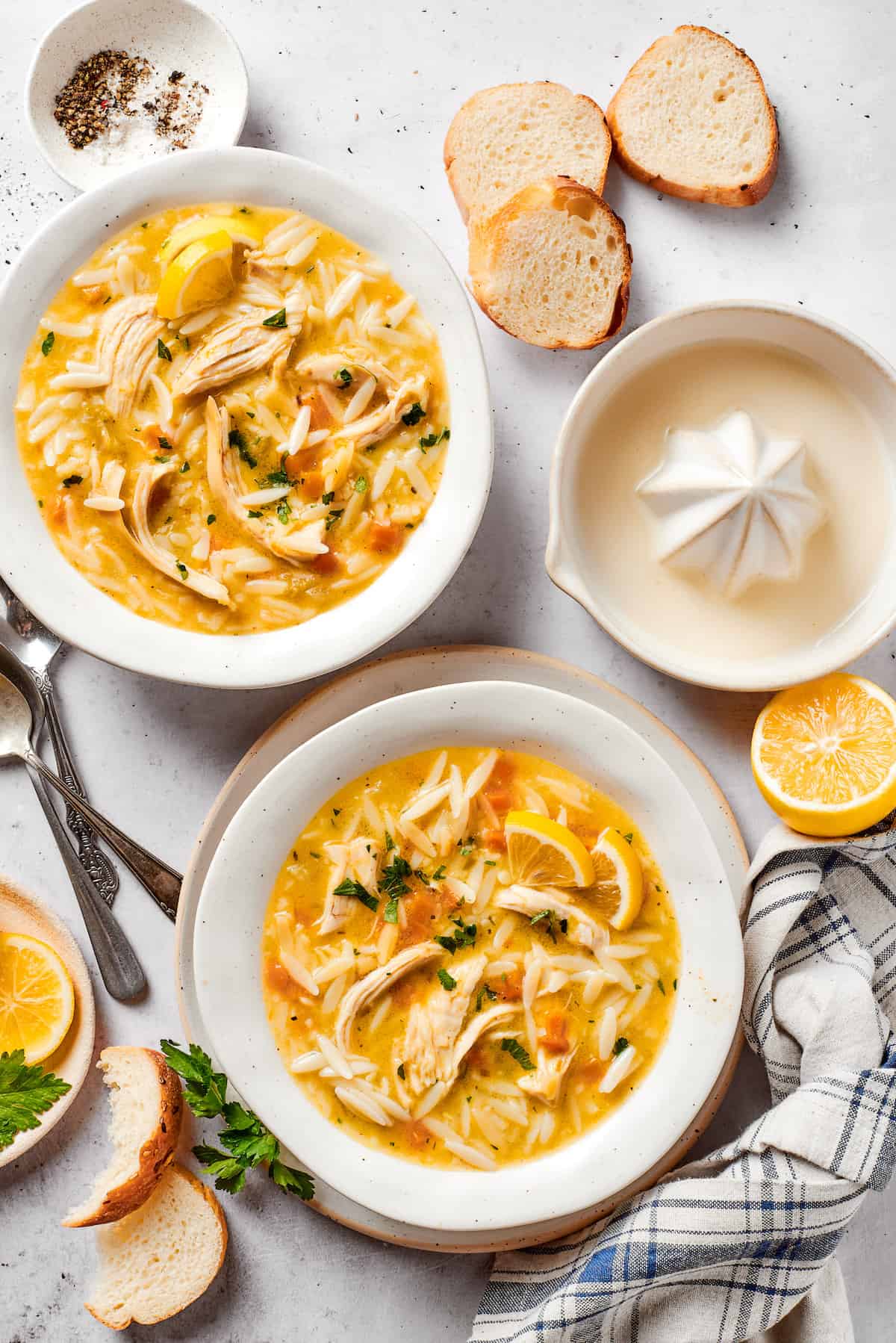 Bowls of lemon chicken orzo soup on a table with a juicer and lemon halves nearby.