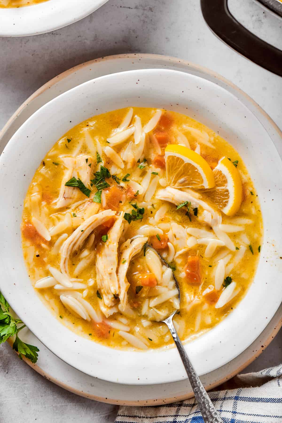 A white bowl brims with lemon chicken orzo soup as a spoon digs in.