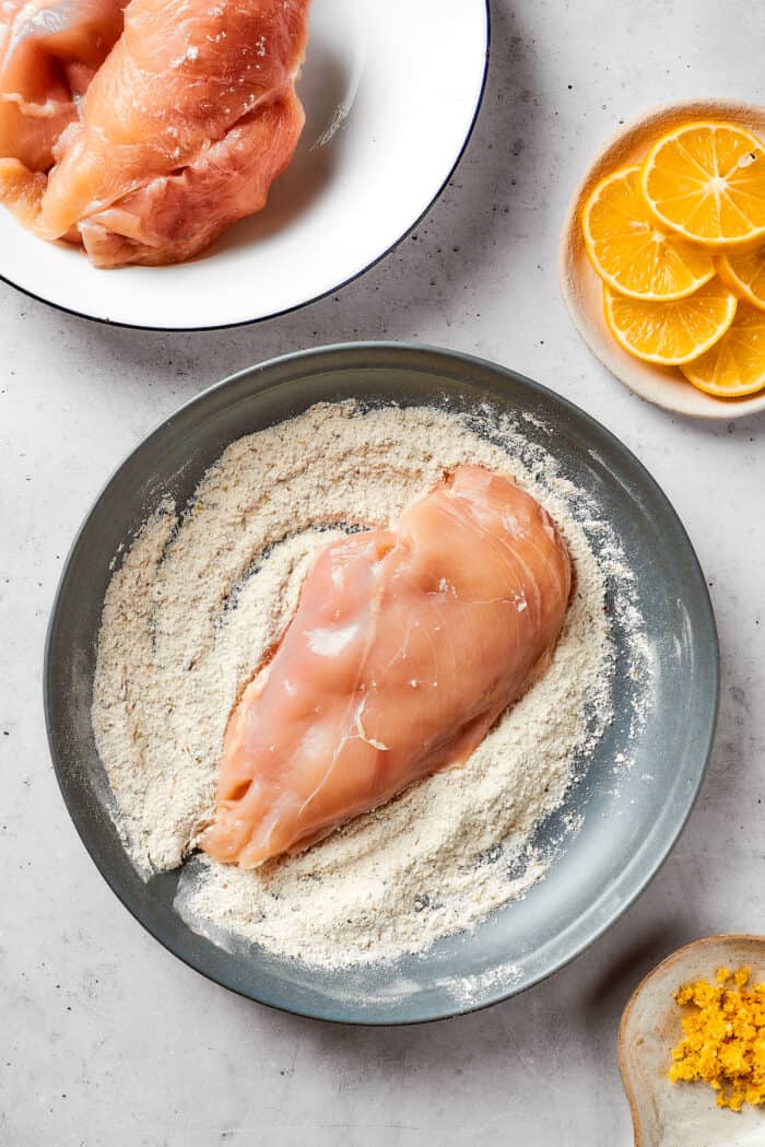 A piece of chicken breast is dredged through a cornstarch mixture.