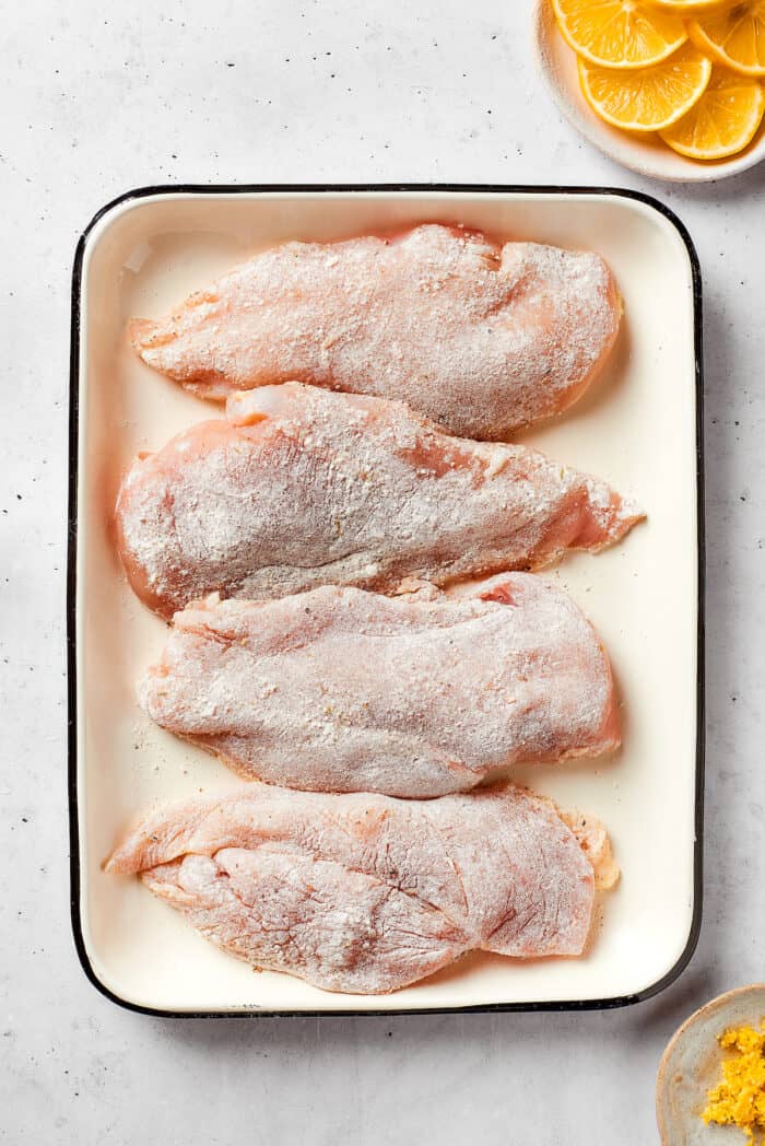 Four pieces of seasoned chicken breast are arranged in a baking dish.