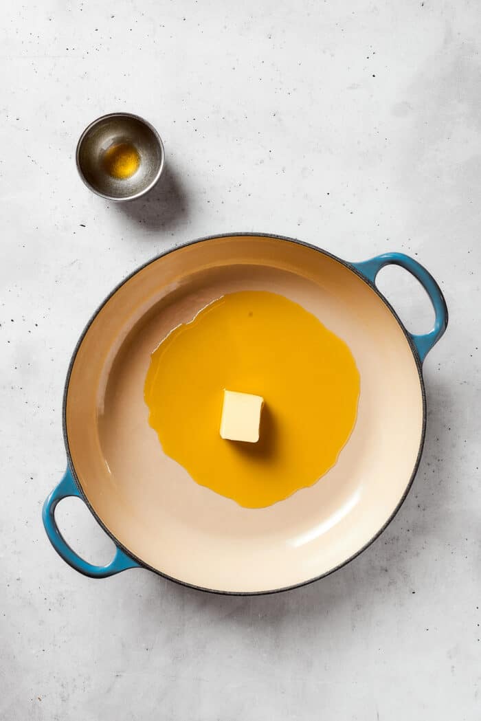 A pat of butter melts into olive oil in a dutch oven.