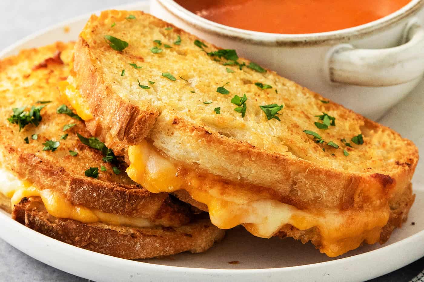 Air fryer grilled cheese sandwiches are shown on a plate along with a bowl of tomato soup.