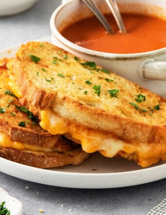 Air fryer grilled cheese sandwiches are shown on a plate along with a bowl of tomato soup.