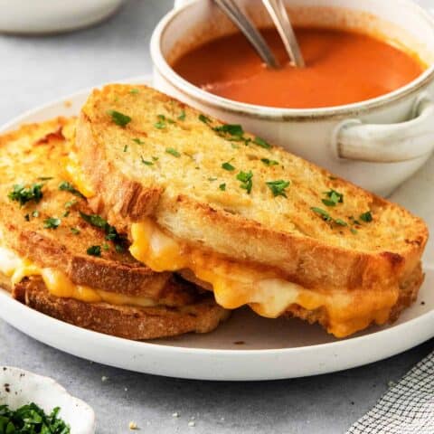 Air fryer grilled cheese sandwiches are shown on a plate along with a bowl of tomato soup.