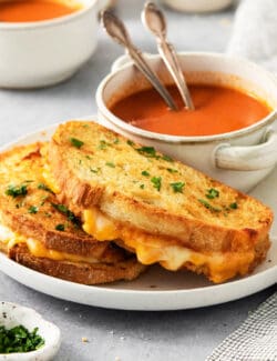 Air fryer grilled cheese sandwiches are shown on a plate along with a bowl of tomato soup.