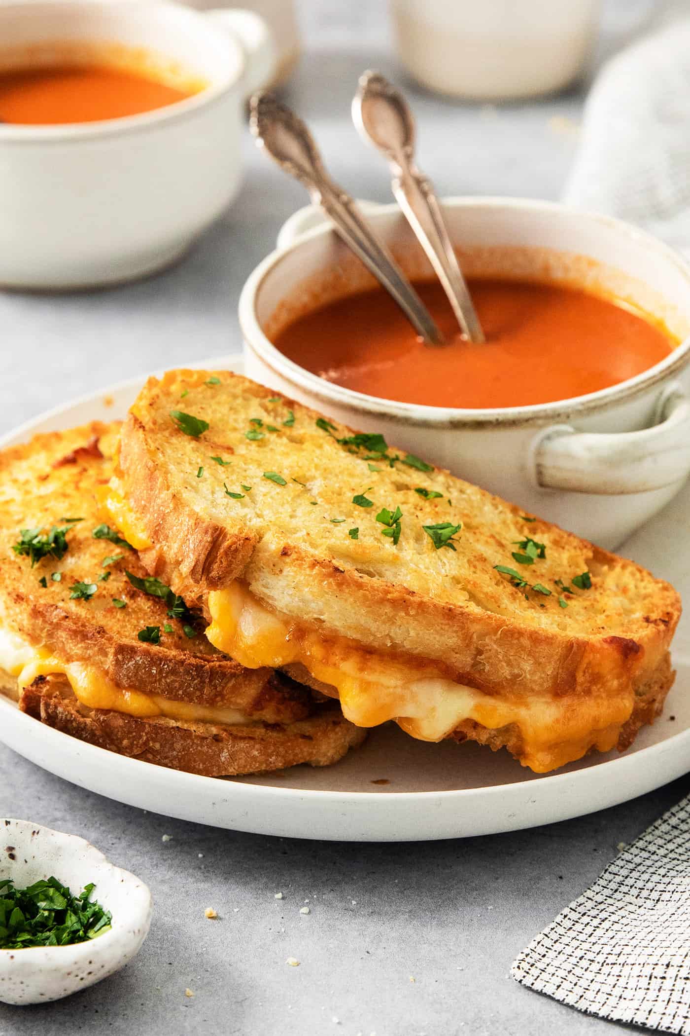 Air fryer grilled cheese sandwiches are shown on a plate along with a bowl of tomato soup.