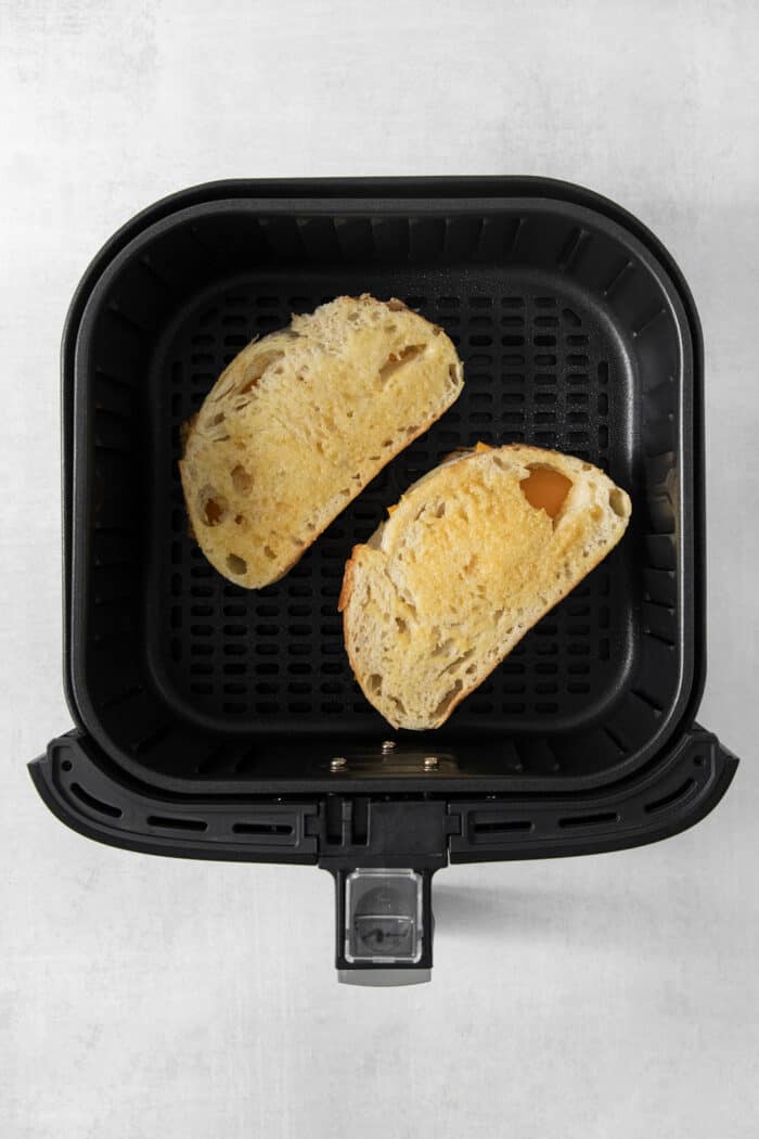 Two grilled cheese sandwiches cook in the air fryer.