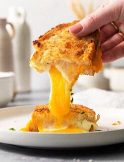 A hand pulls apart a piece of air fryer grilled cheese to show the melted cheese inside.