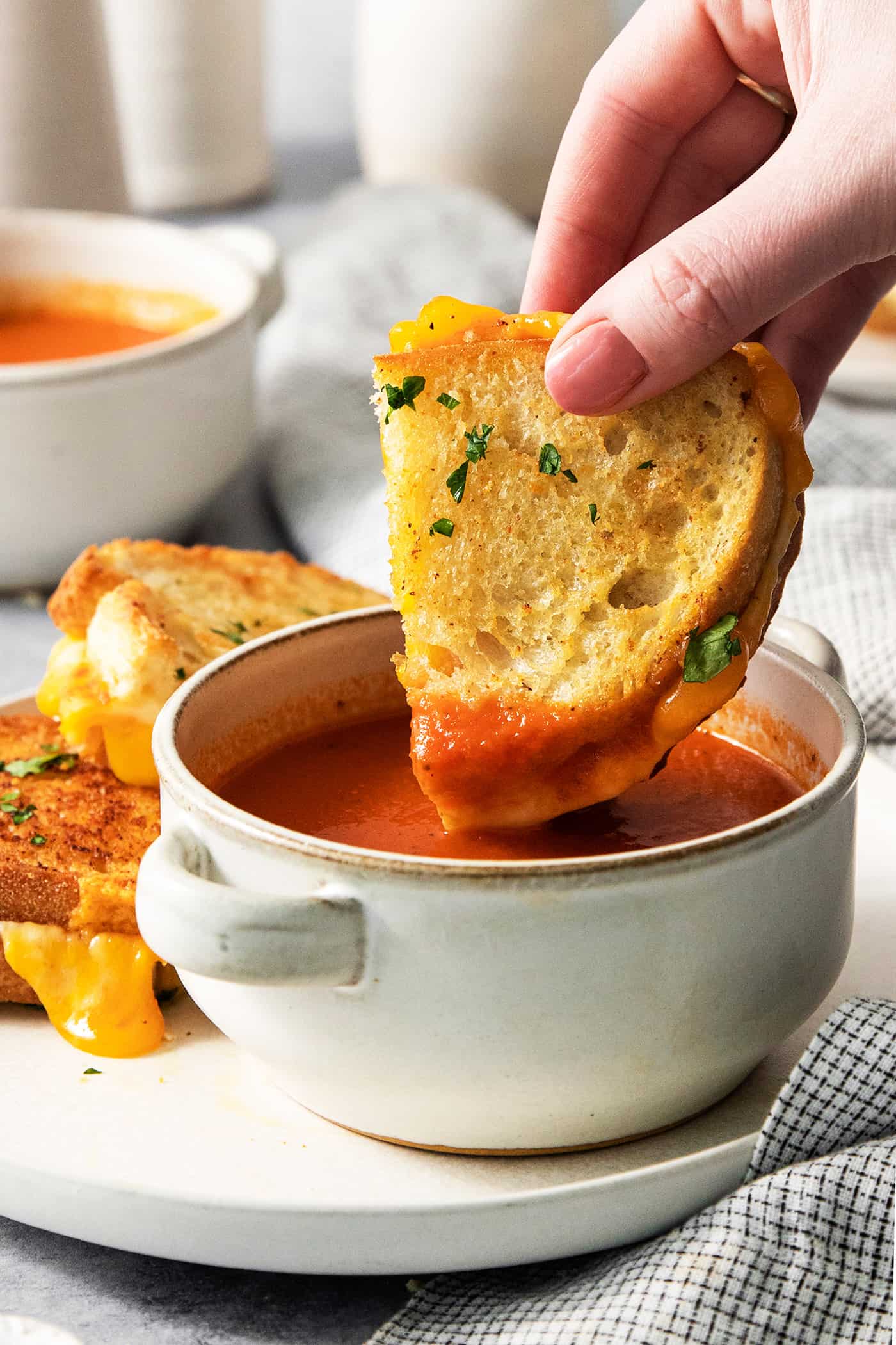 A hand dips a piece of air fryer grilled cheese into a small bowl of tomato soup.