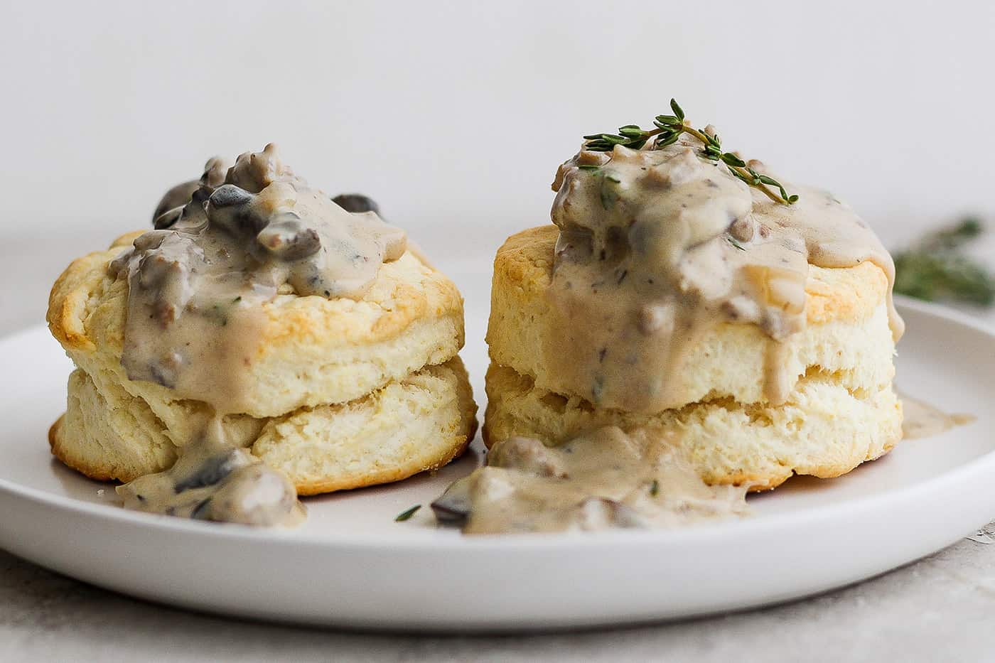 Two cream biscuits on a white plate topped with sausage and mushroom gravy.