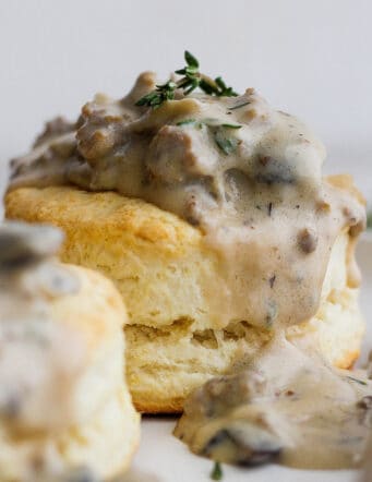 Two cream biscuits on a white plate topped with sausage and mushroom gravy.
