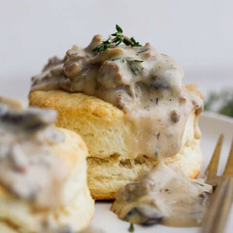 Two cream biscuits on a white plate topped with sausage and mushroom gravy.