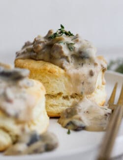 Two cream biscuits on a white plate topped with sausage and mushroom gravy.