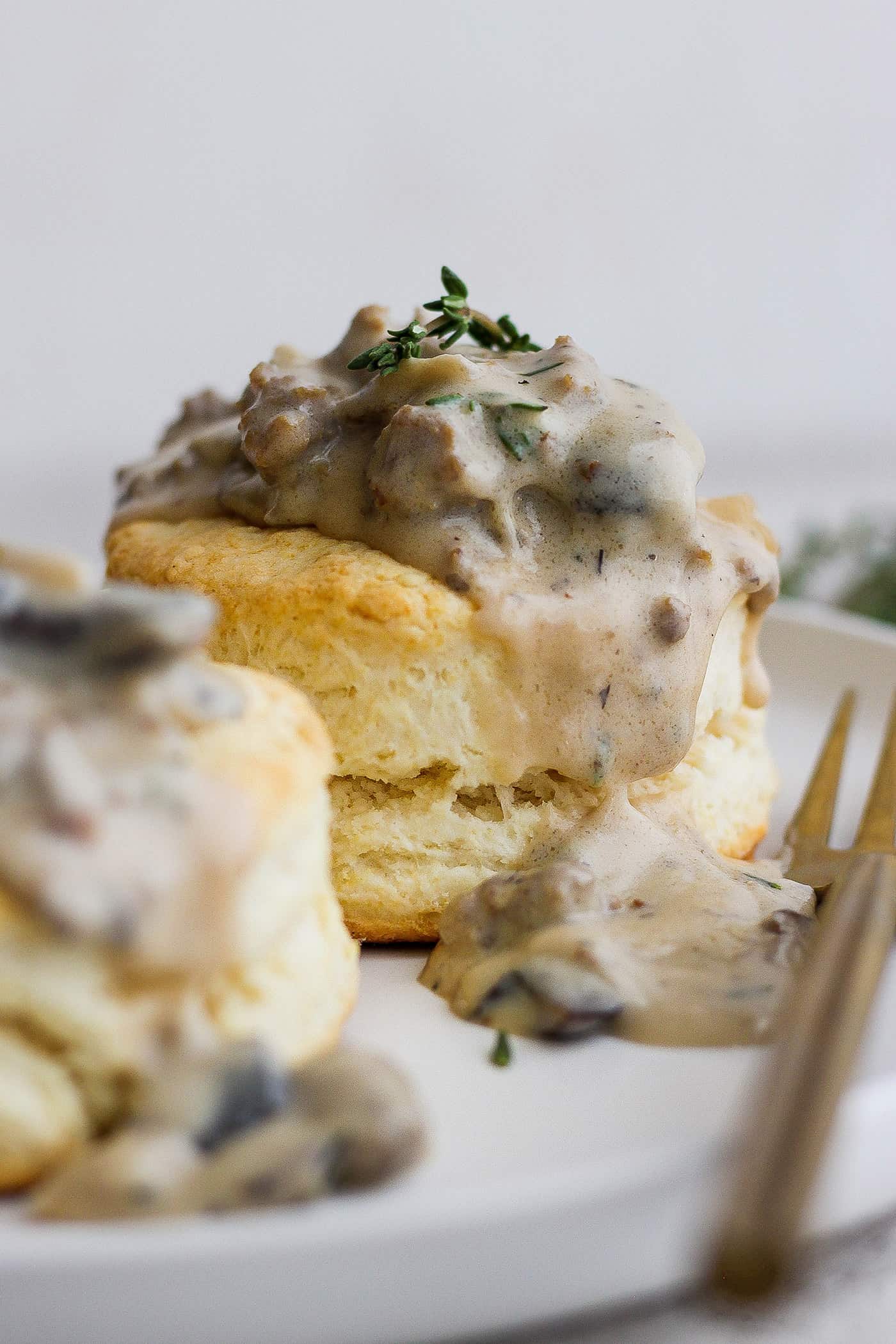 Two cream biscuits on a white plate topped with sausage and mushroom gravy.