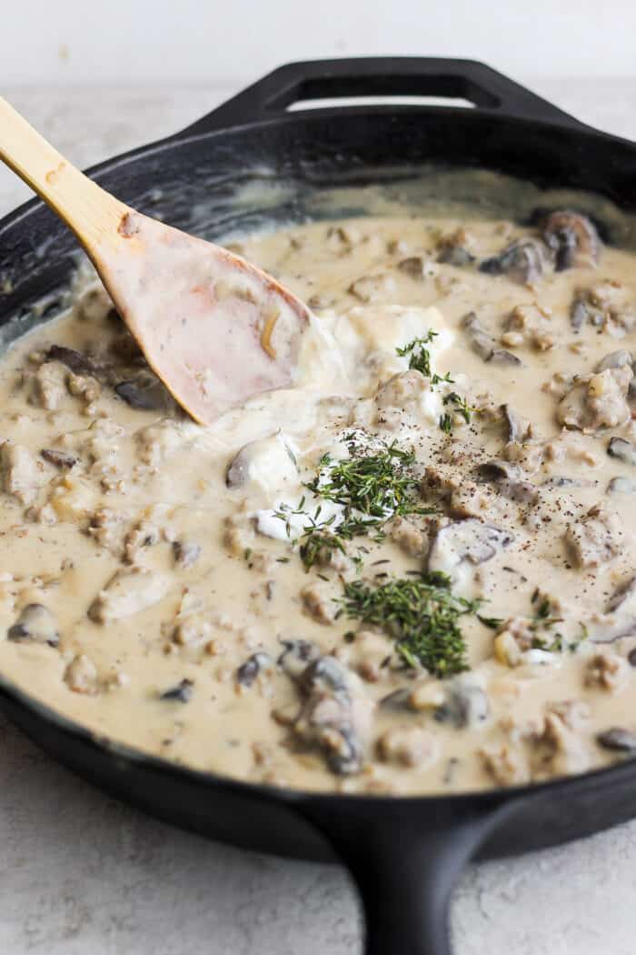 A creamy skillet of sausage gravy is stirred with a wooden spoon.