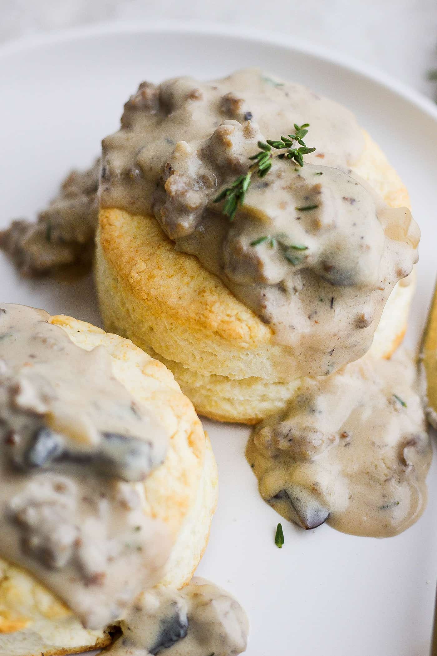 Two cream biscuits on a white plate topped with sausage and mushroom gravy.