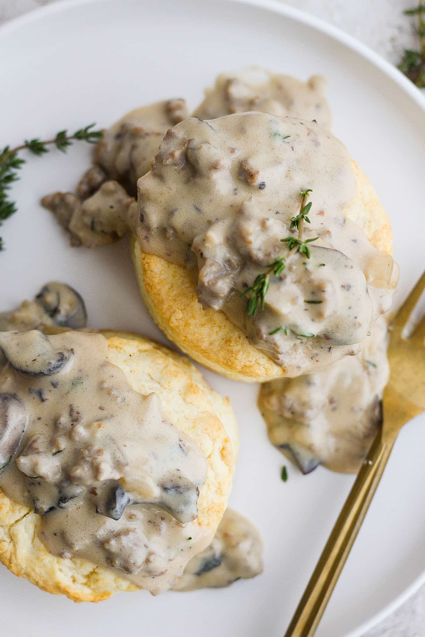 A fork rests on a plate of two cream biscuits topped with sausage gravy.