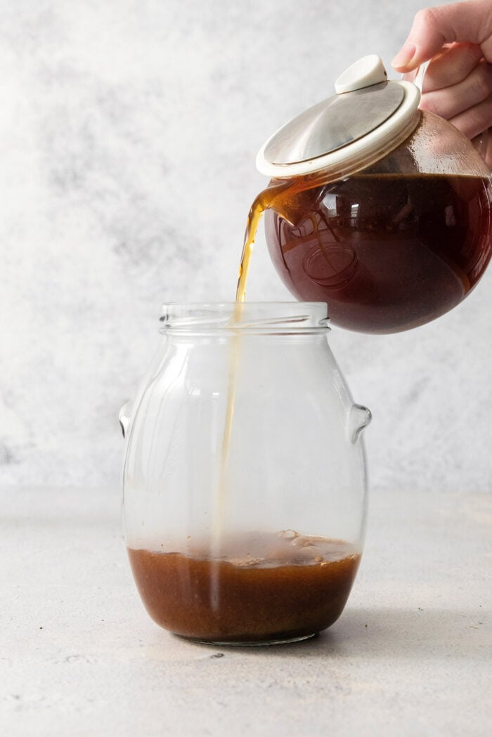 pouring steeped tea into a large jar