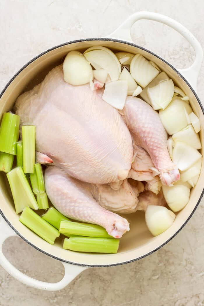 A whole chicken cooks in a pot of water with onions and celery to make chicken stock.