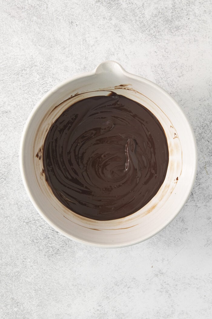 Chocolate melts into hot cream in a white bowl.