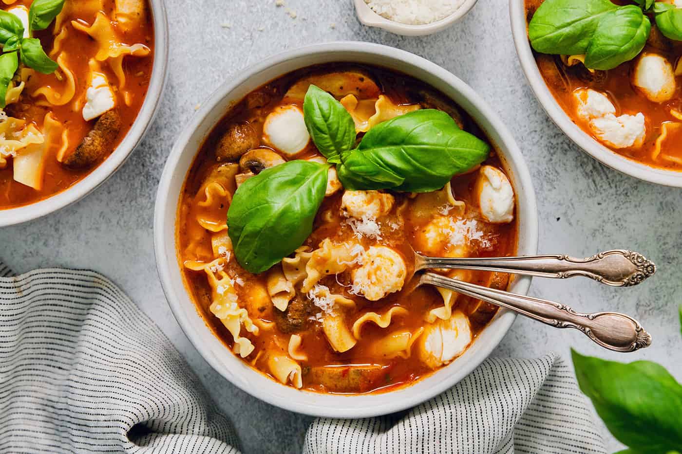 Fresh basil leaves garnish a bowl of slow cooker lasagna soup with chicken.