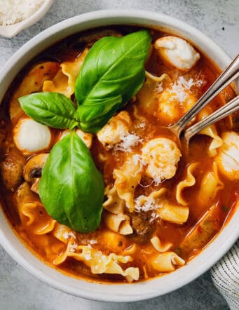 Fresh basil leaves garnish a bowl of slow cooker lasagna soup with chicken.