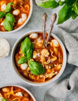 Two spoons stick out of a bowl of slow cooker lasagna soup with chicken.