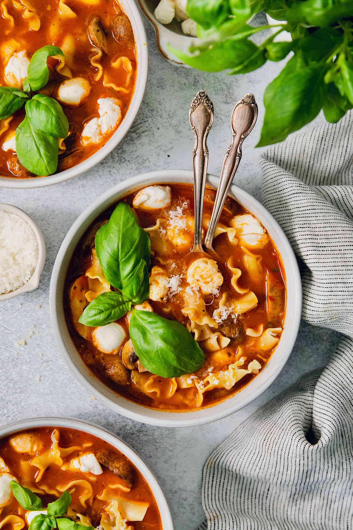 Two spoons stick out of a bowl of slow cooker lasagna soup with chicken.