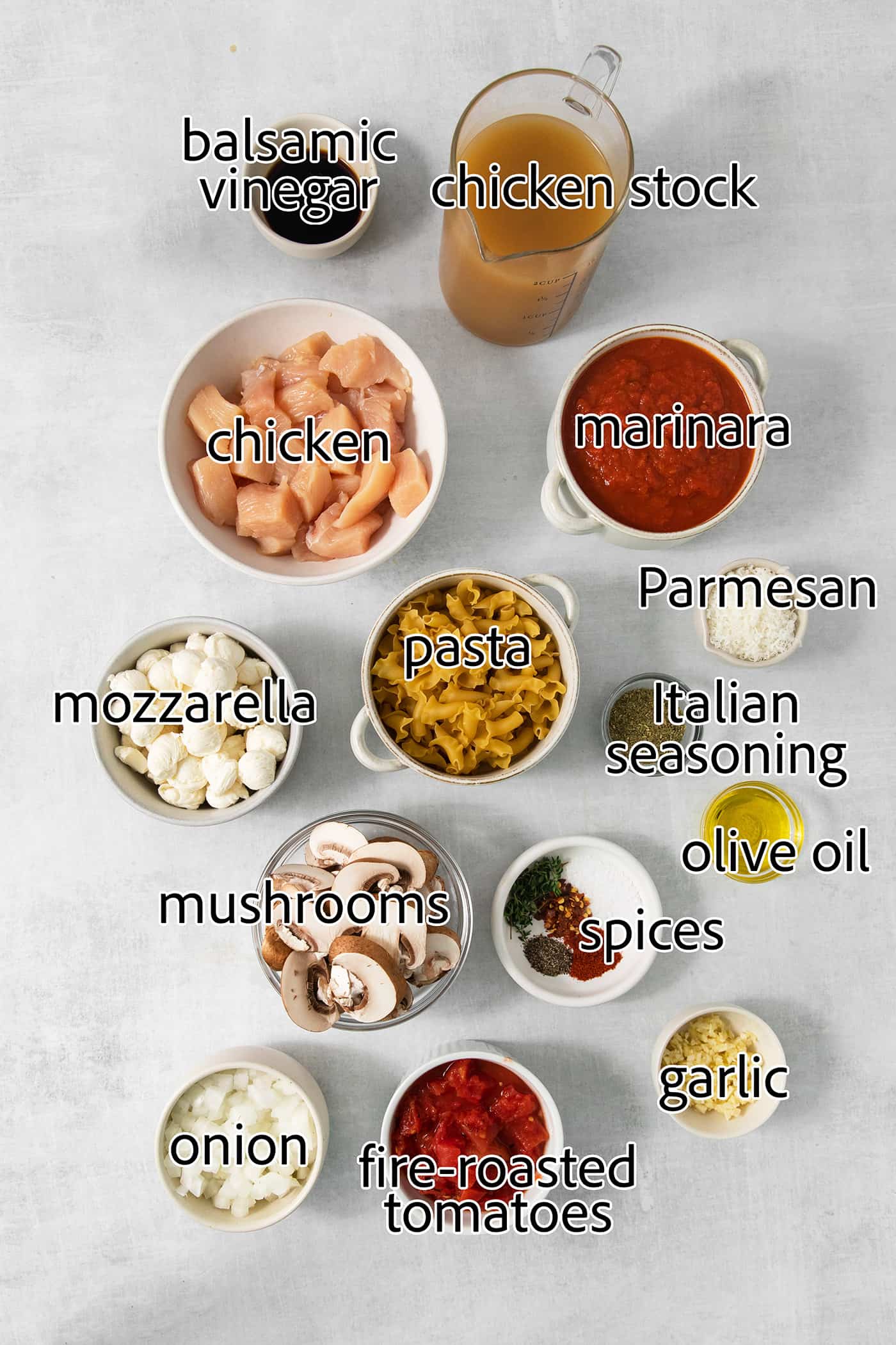 The ingredients for slow cooker lasagna soup are shown: chicken, canned tomatoes, spices, red pepper flakes, fresh mozzarella, parmesan, pasta, chicken broth, olive oil, garlic, mushrooms, salt and pepper.