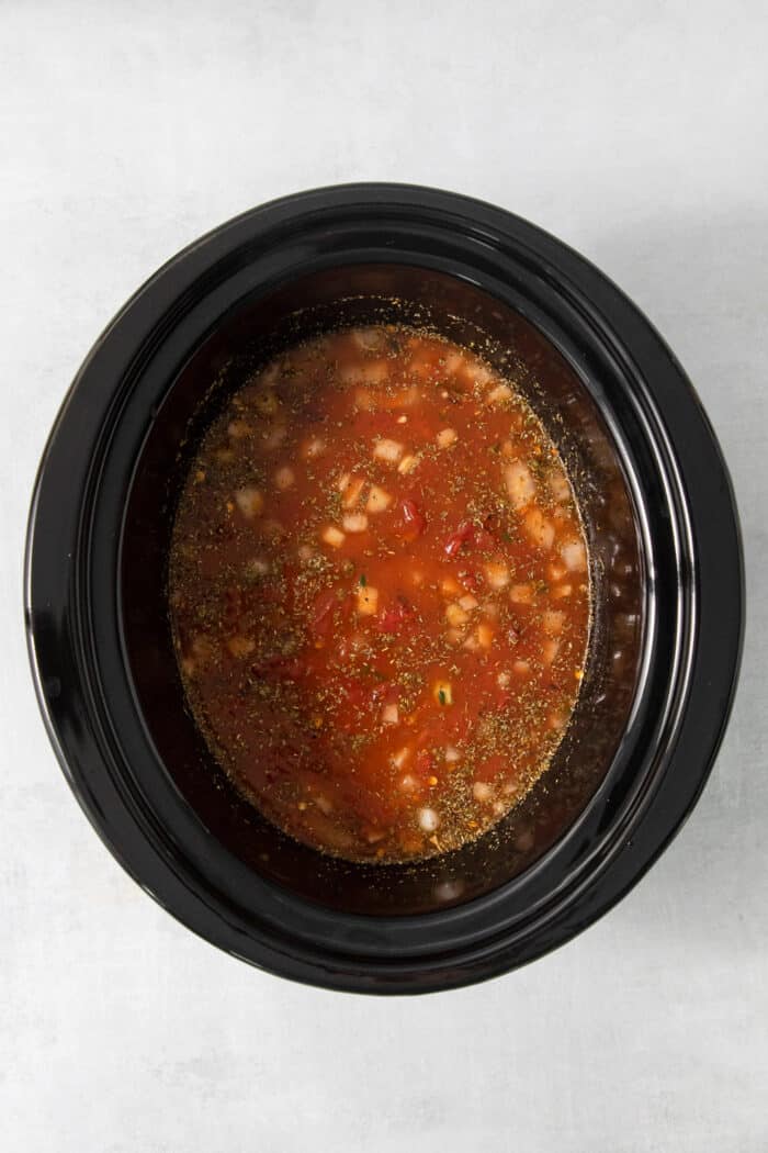 Vegetables, broth, and tomatoes added to a slow cooker.