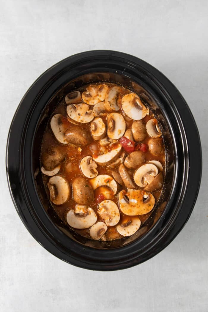 Mushrooms are seen atop the rest of the ingredients for slow cooker lasagna soup.