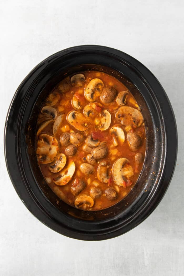 Mushrooms cook in a b broth and tomato mixture in the slow cooker.