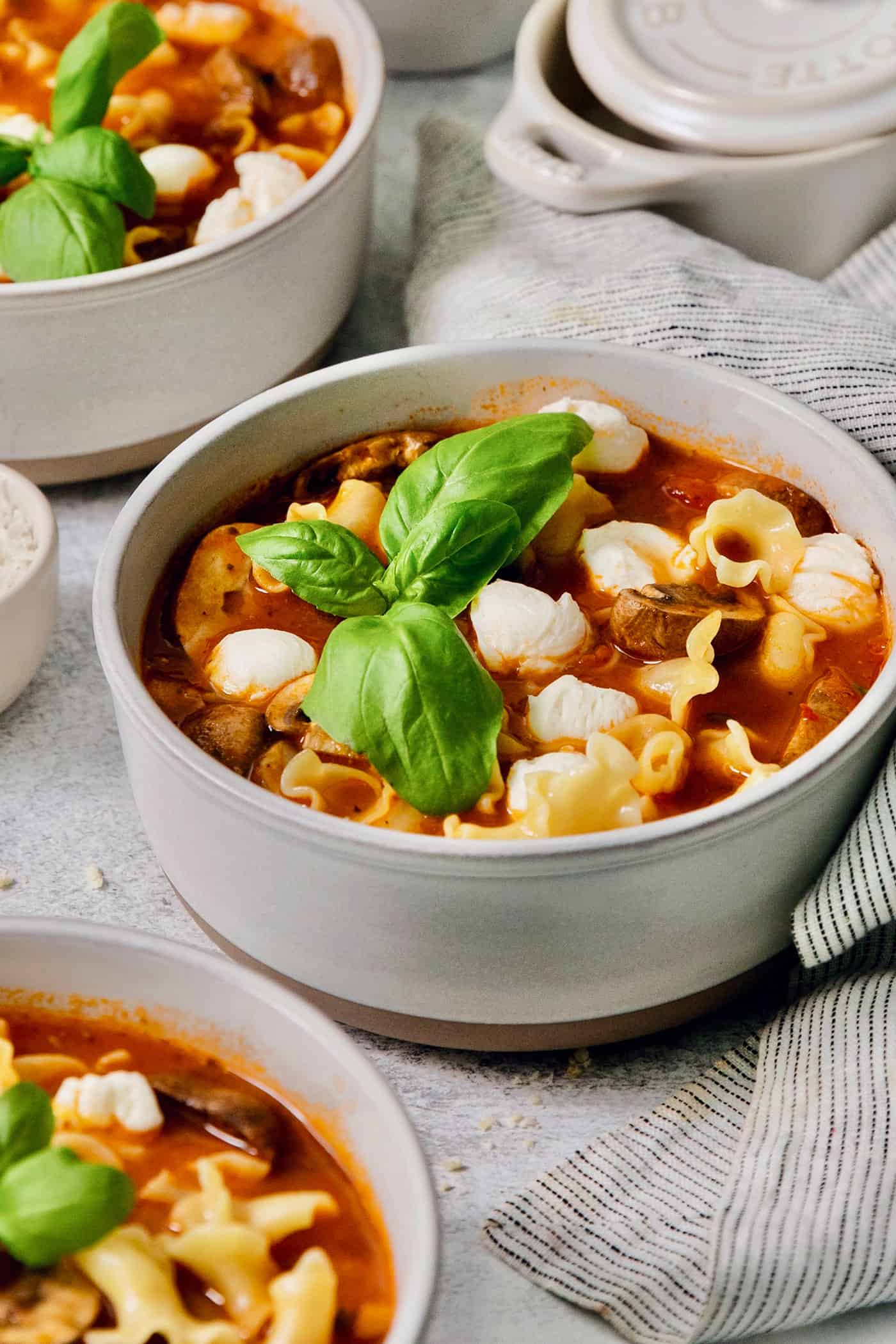 Fresh basil leaves garnish a bowl of slow cooker lasagna soup with chicken.