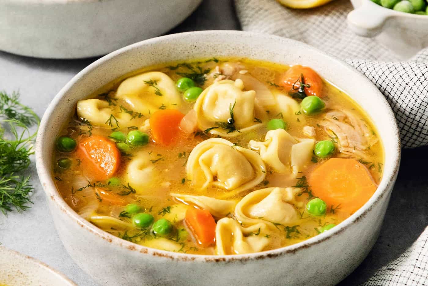 A bowl of lemon chicken tortellini soup showing peas, carrots, and torellini.