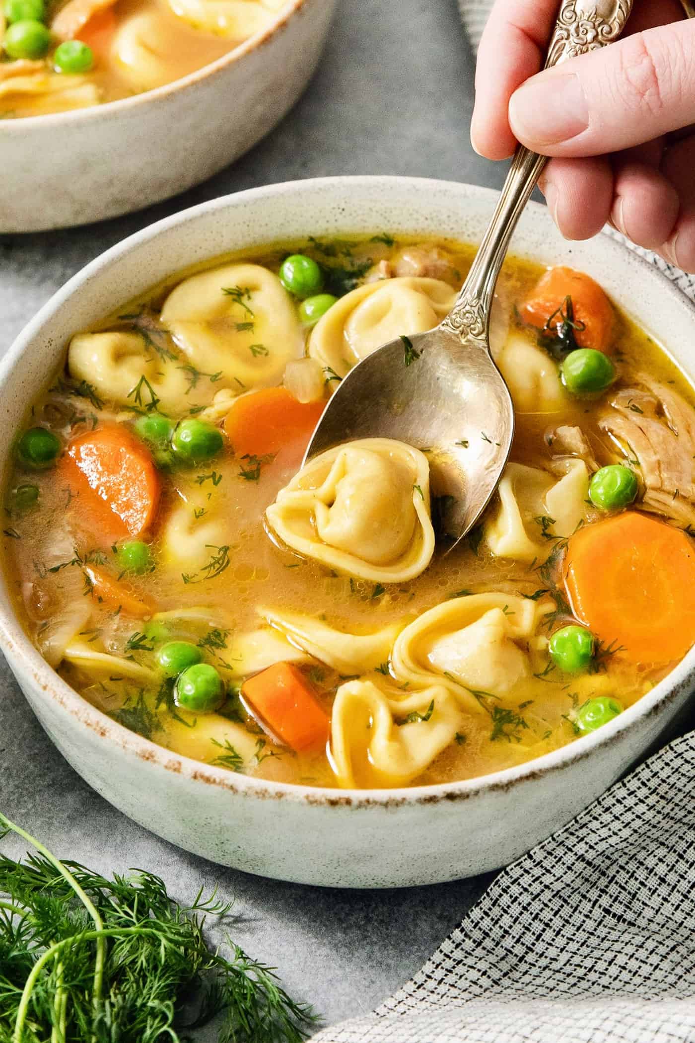 A spoon lifts a tortellini out of a bowl of lemon chicken tortellini soup.