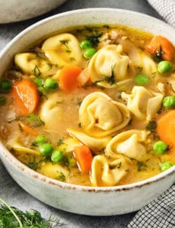 A bowl of lemon chicken tortellini soup showing peas, carrots, and torellini.