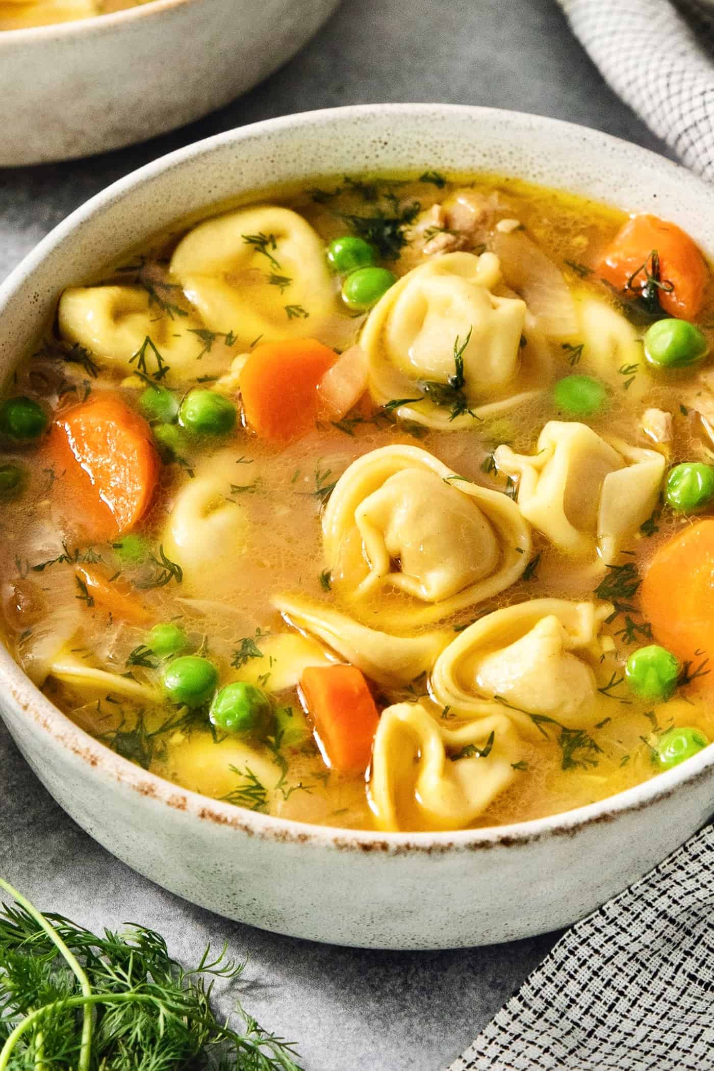 A bowl of lemon chicken tortellini soup showing peas, carrots, and torellini.