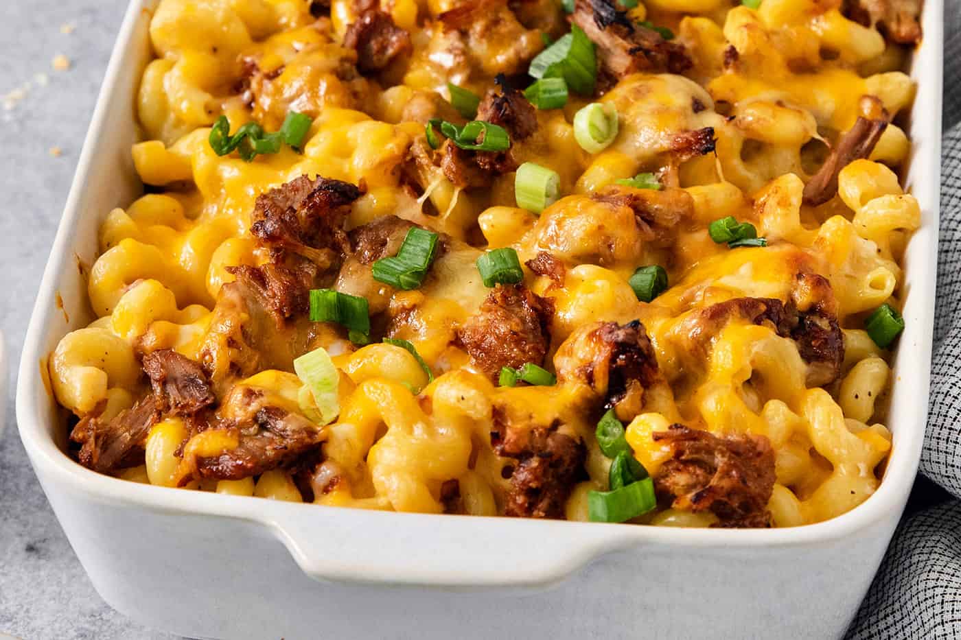 A green onion-topped casserole dish full of cooked pulled pork mac and cheese.
