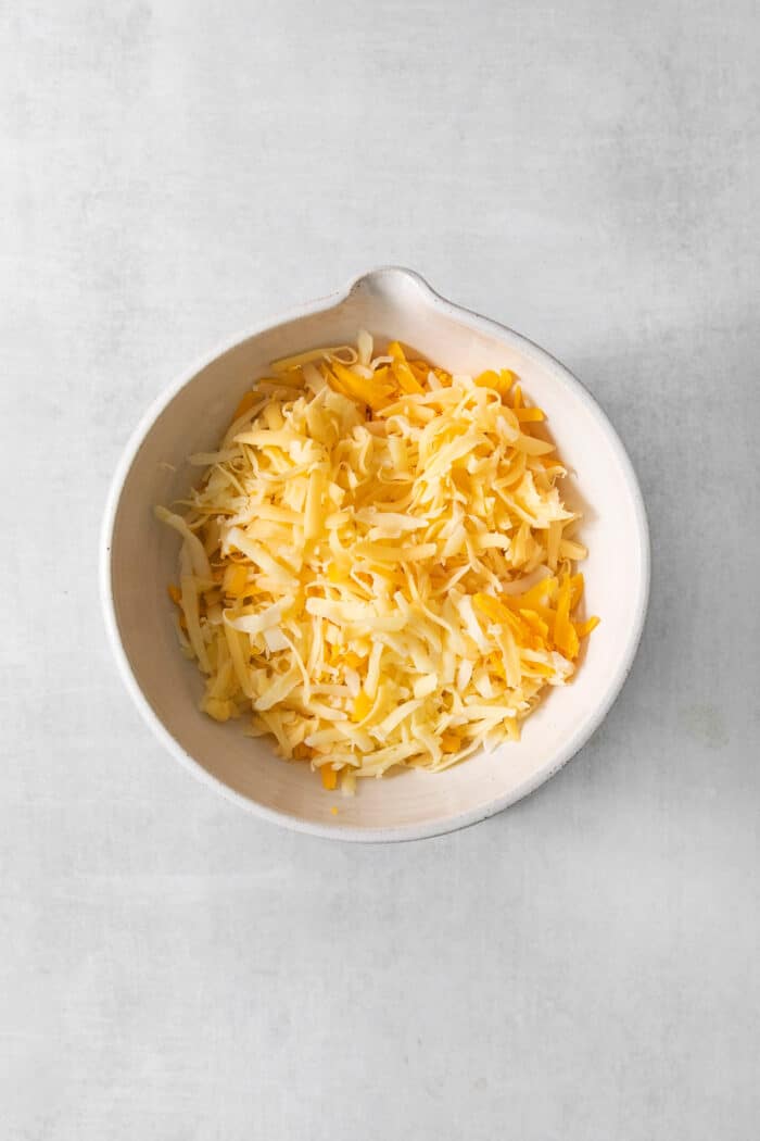 Shredded gouda, fontina, and cheddar cheeses in a white bowl.