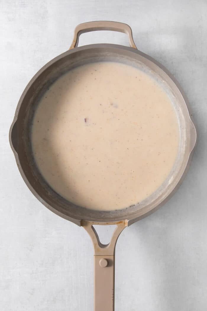 Flour, butter, and milk cook in a pot to form a roux.