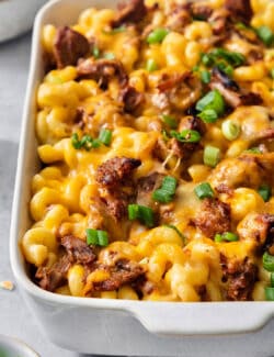 A side view of a white casserole dish full of pulled pork mac and cheese topped with green onions.