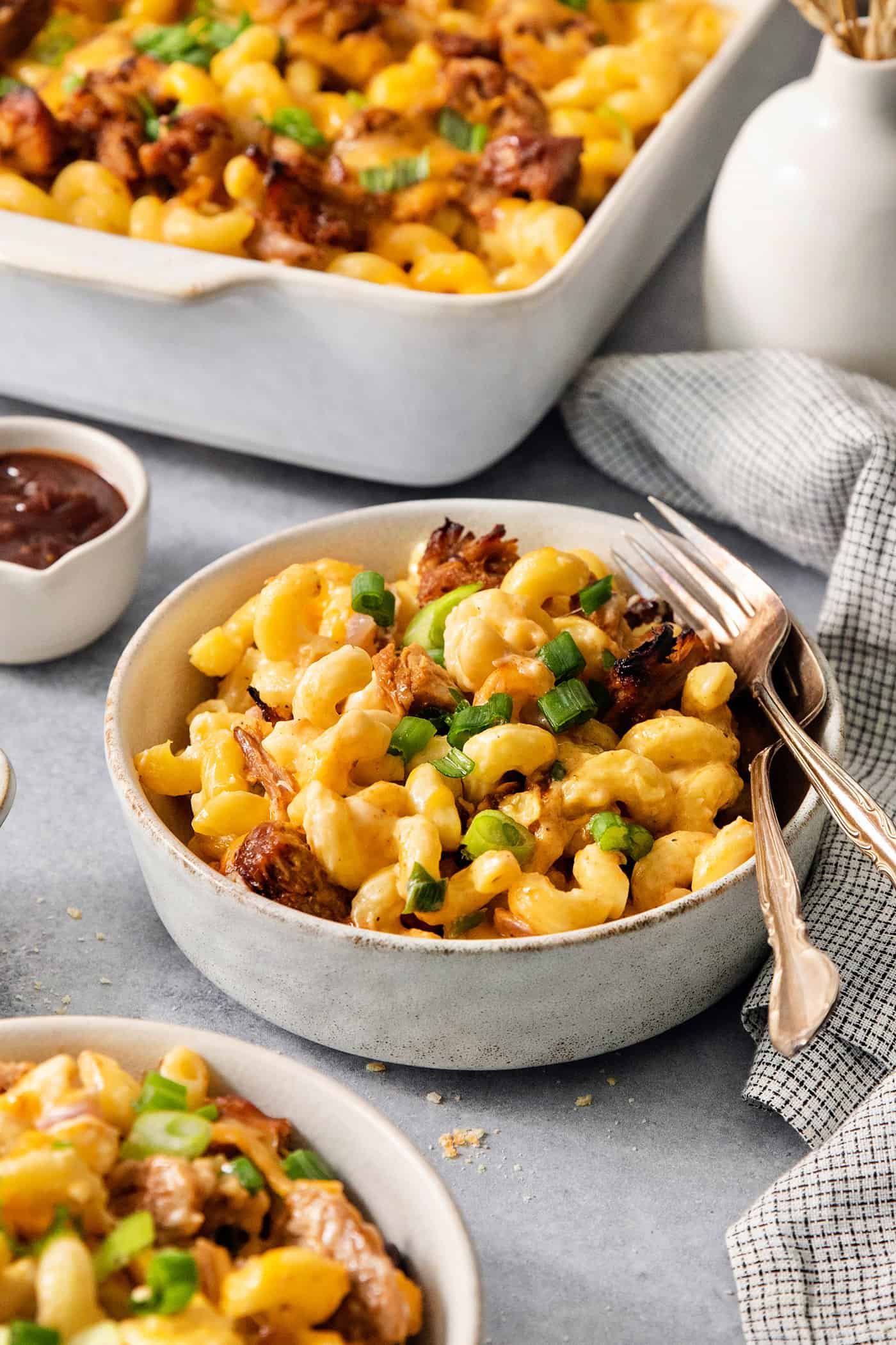 Bowls of pulled pork and cheese on a table with a pan of mac and cheese in the background.