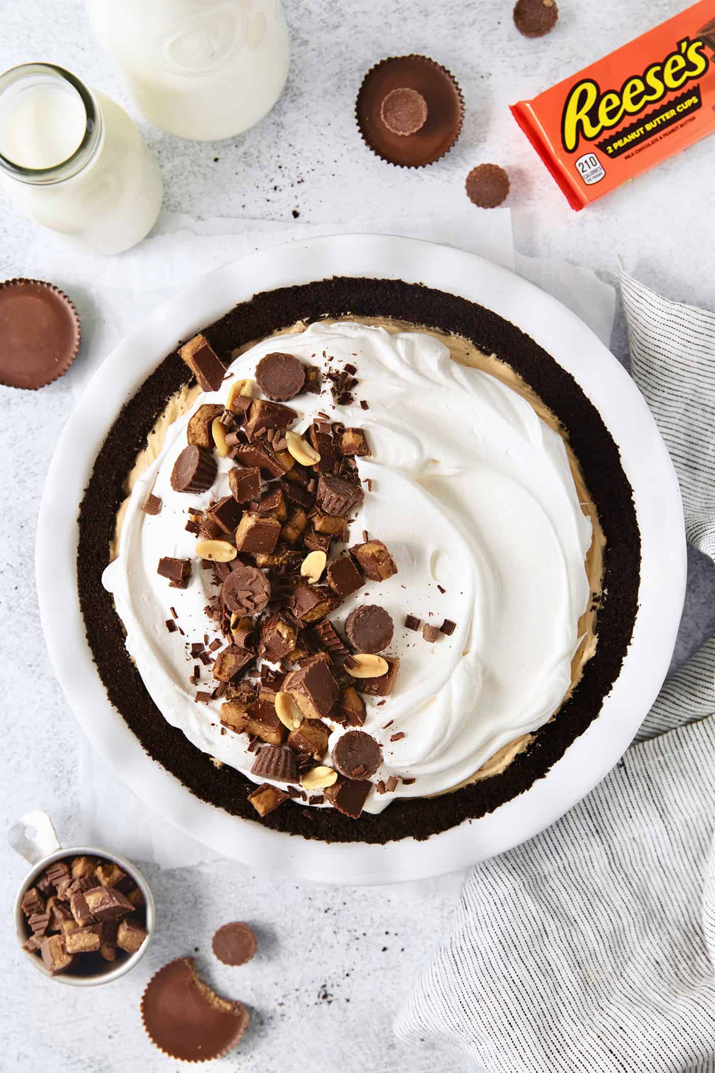This no-bake Reese’s Pie features a crisp Oreo crust and a creamy peanut butter filling finished with whipped topping and Reese’s cups. A whole Reeses pie on a white background with a package of peanut butter cups.