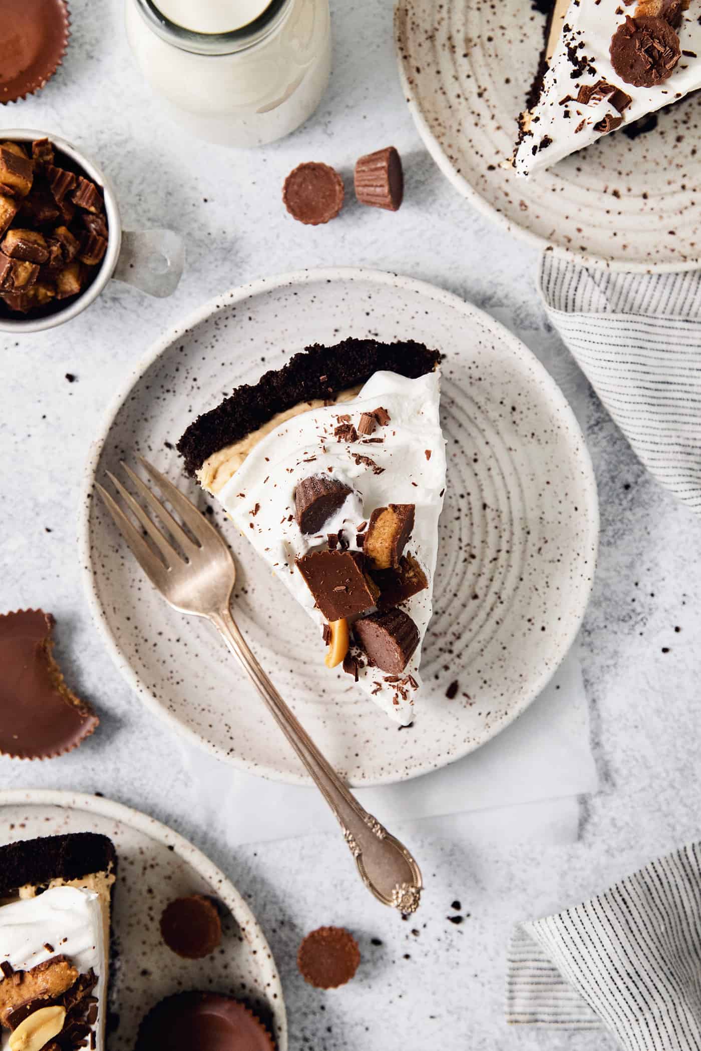 A slice of Reeses pie on a plate with a fork, topped with chopped peanut butter cups.