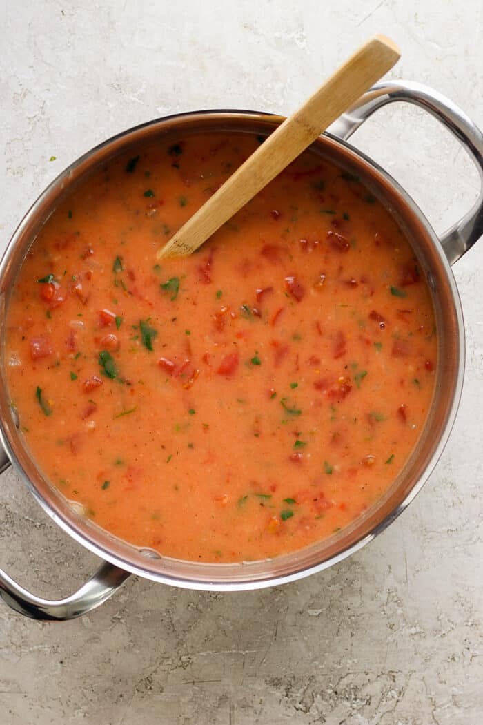 A wooden spoon stirs in the tomatoes for tomato bisque.