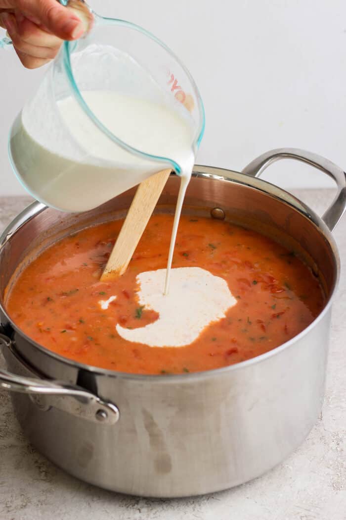 Cream is poured into the soup pot from a glass measuring cup.